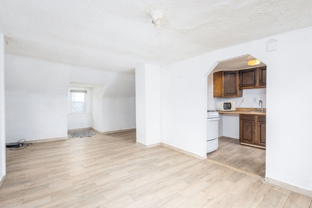 kitchen featuring light countertops, a sink, a textured ceiling, light wood-type flooring, and white appliances