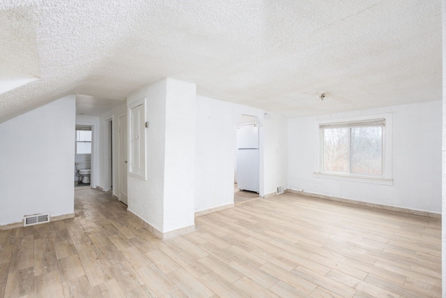 interior space featuring baseboards, visible vents, a textured ceiling, and light wood finished floors