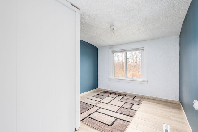 spare room featuring visible vents, a textured ceiling, baseboards, and wood finished floors