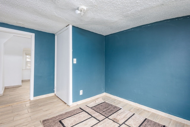 spare room with a textured ceiling, baseboards, and wood finished floors