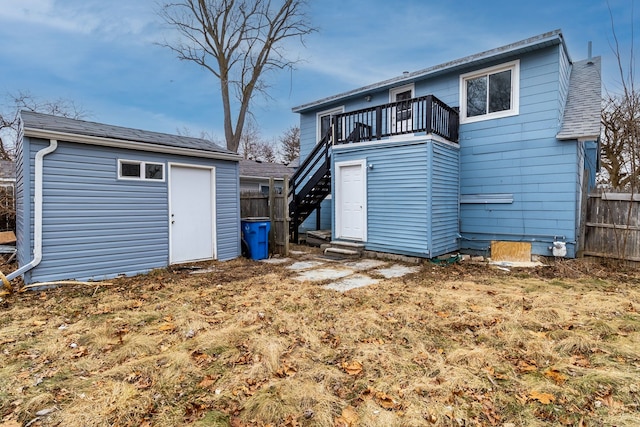 rear view of property with a balcony, roof with shingles, fence, and an outdoor structure