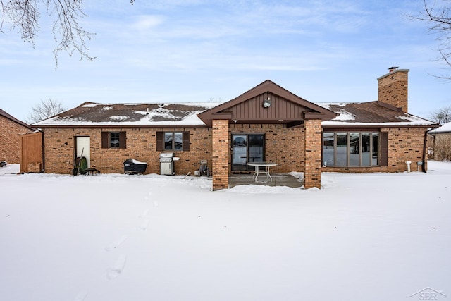 snow covered rear of property featuring brick siding and a chimney