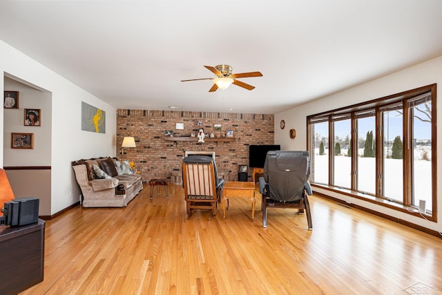 living room with light wood-style floors, brick wall, a brick fireplace, and a ceiling fan