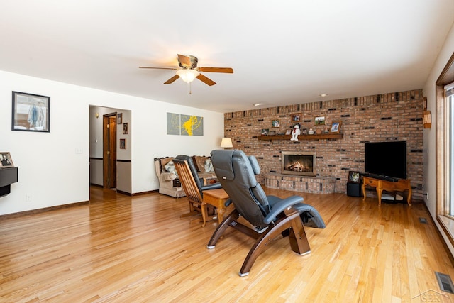 living room featuring baseboards, a brick fireplace, a ceiling fan, and light wood-style floors