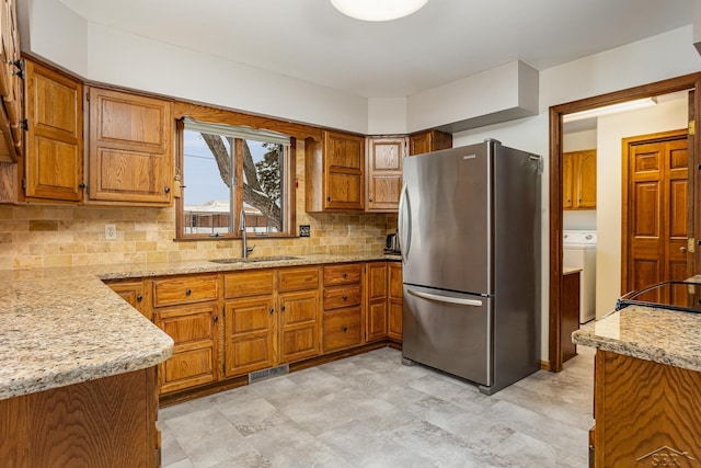 kitchen featuring light stone counters, freestanding refrigerator, brown cabinets, and a sink