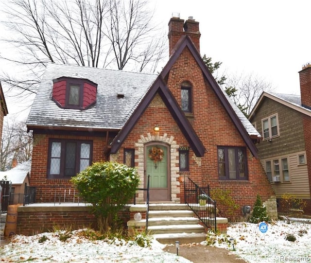 tudor home with entry steps, brick siding, and a chimney