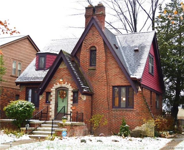 tudor house with brick siding, a chimney, and roof with shingles