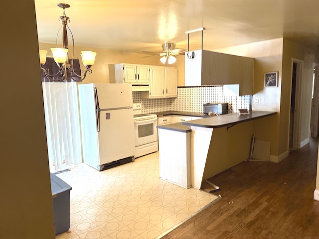 kitchen with a peninsula, white appliances, hanging light fixtures, decorative backsplash, and dark countertops