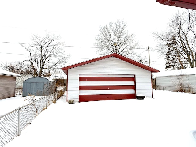 snow covered garage with a detached garage and fence