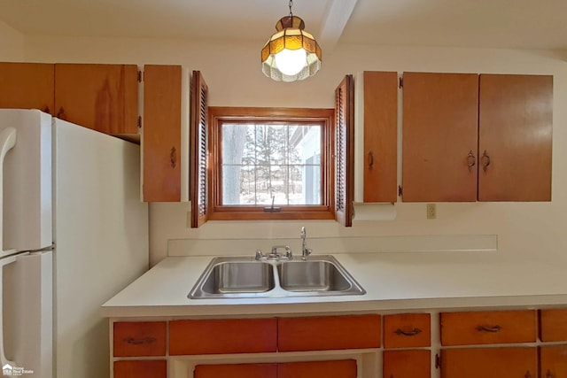 kitchen featuring hanging light fixtures, light countertops, a sink, and freestanding refrigerator