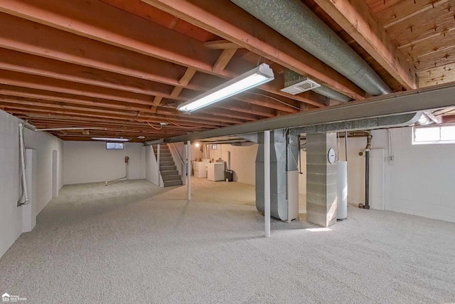 below grade area featuring gas water heater, heating unit, visible vents, stairway, and washing machine and dryer