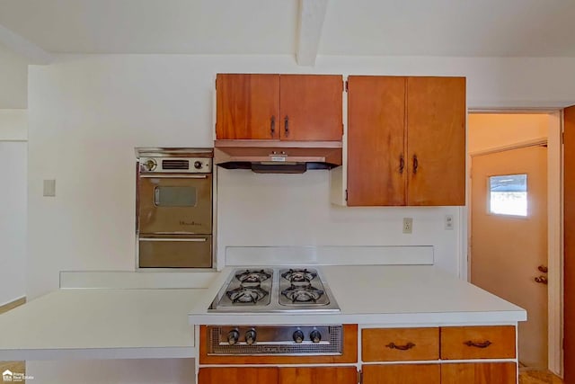 kitchen with appliances with stainless steel finishes, light countertops, under cabinet range hood, beam ceiling, and a warming drawer