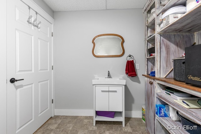 bathroom with baseboards, a drop ceiling, and vanity