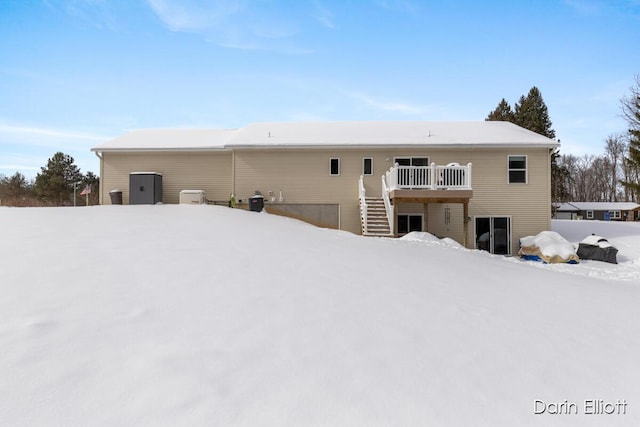 snow covered rear of property with a deck and stairway