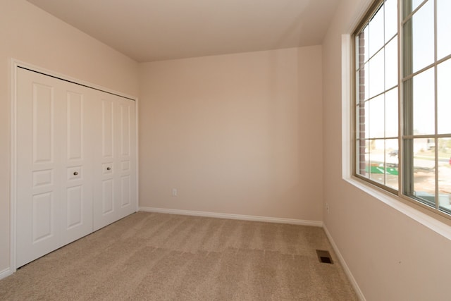 unfurnished bedroom featuring baseboards, a closet, visible vents, and light colored carpet