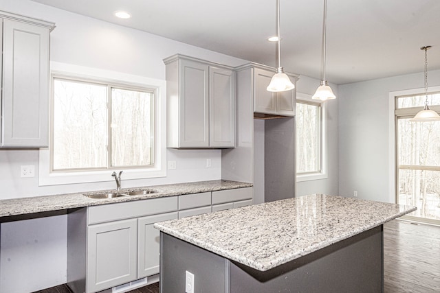 kitchen with a kitchen island, light stone counters, a sink, and decorative light fixtures