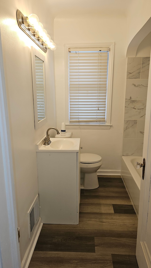 bathroom with toilet, wood finished floors, vanity, visible vents, and a bath