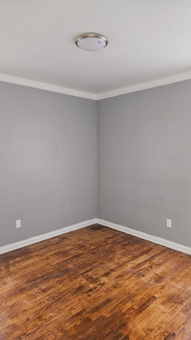 empty room with ornamental molding, baseboards, and wood finished floors