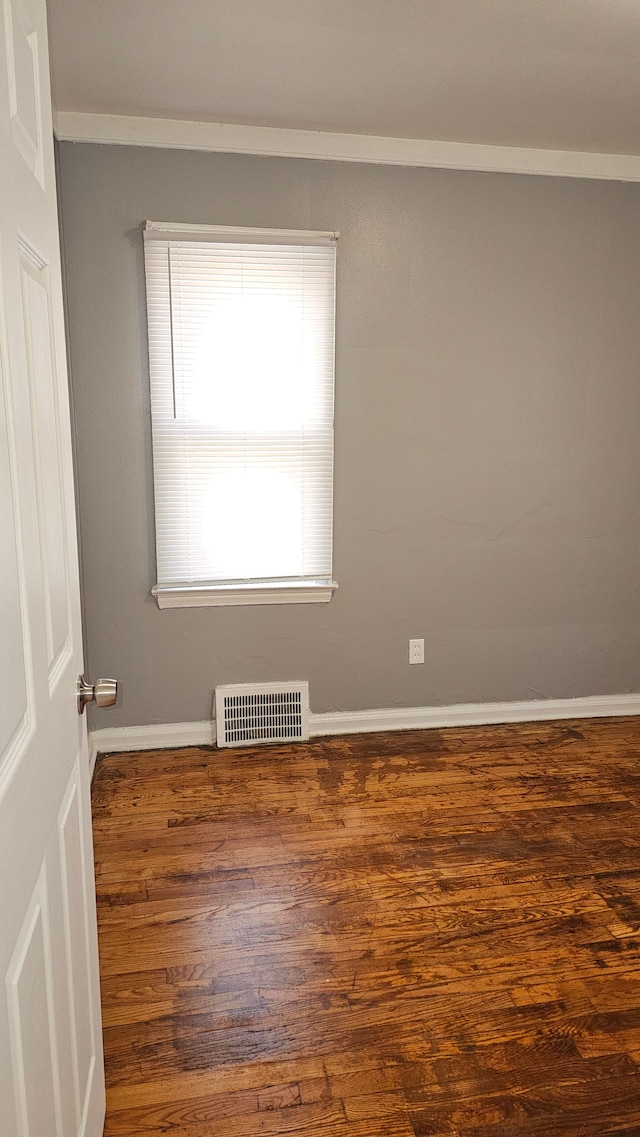 empty room featuring crown molding, dark wood-style flooring, visible vents, and baseboards