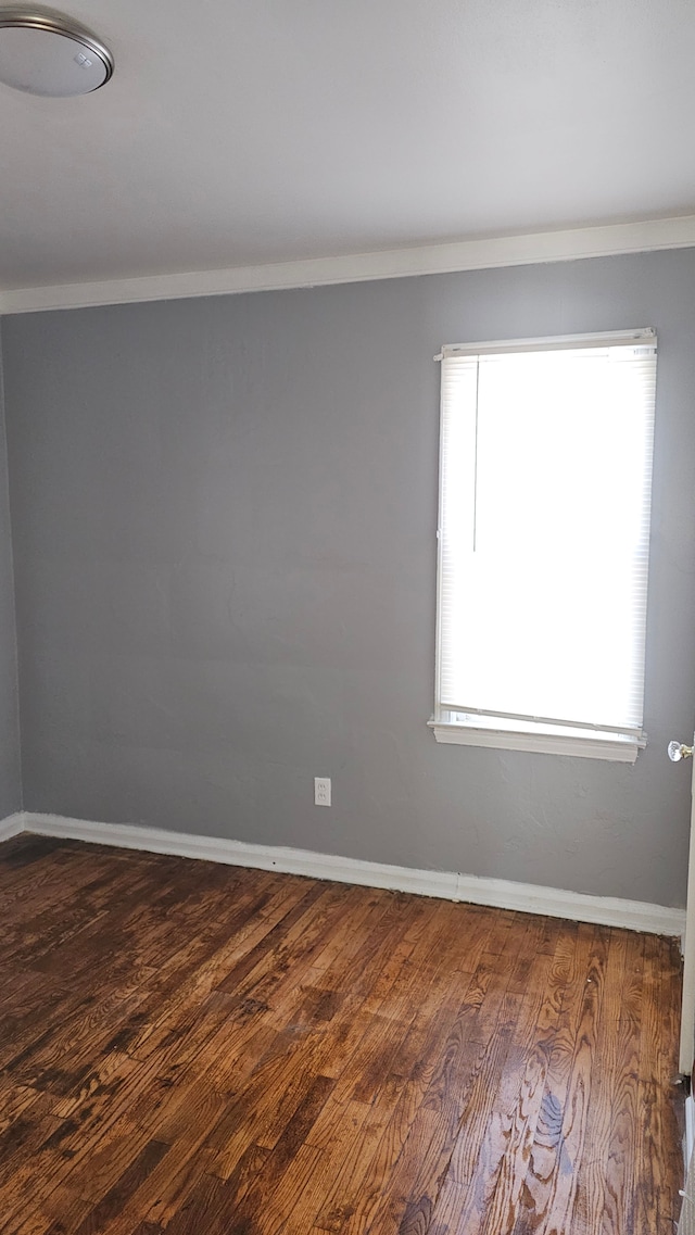 spare room with crown molding, dark wood finished floors, and baseboards