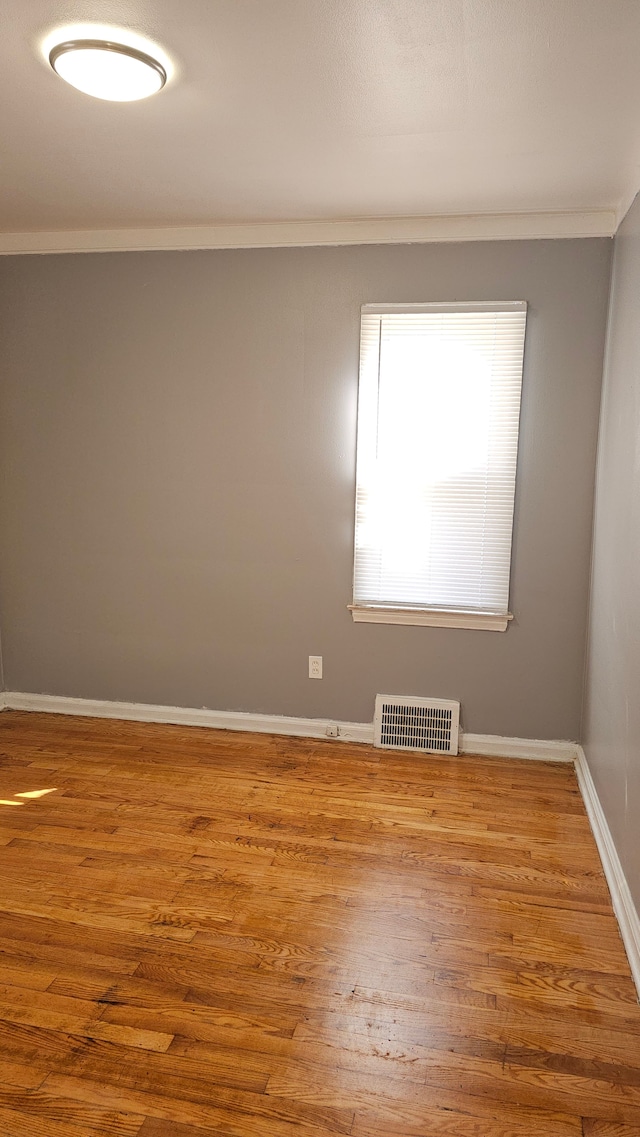 unfurnished room with ornamental molding, wood finished floors, visible vents, and baseboards