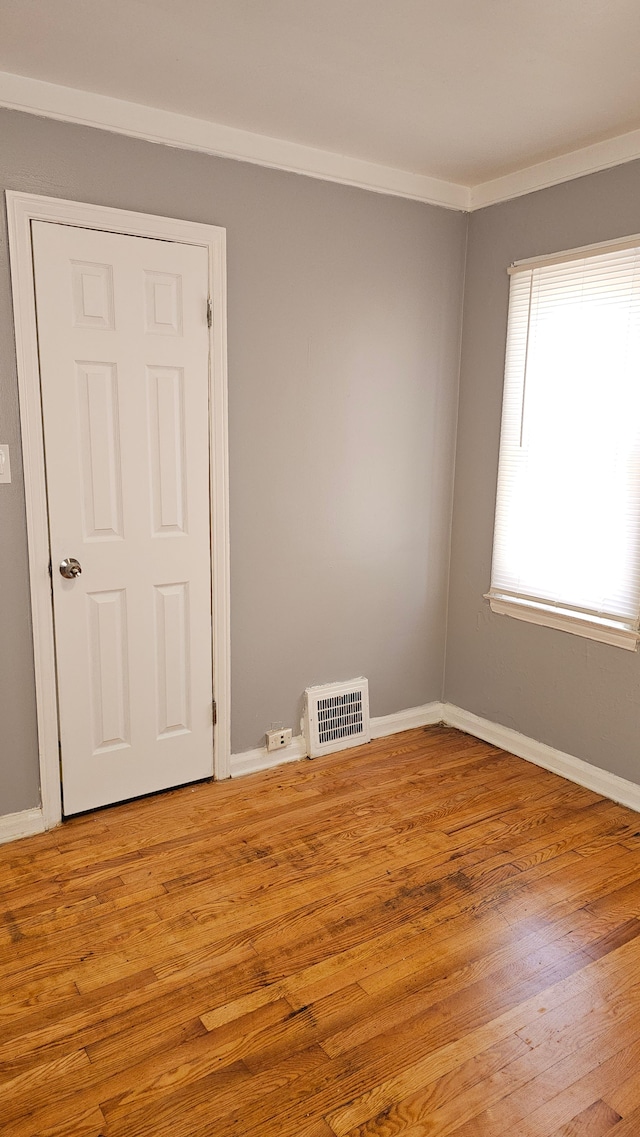 empty room with ornamental molding, baseboards, visible vents, and light wood finished floors