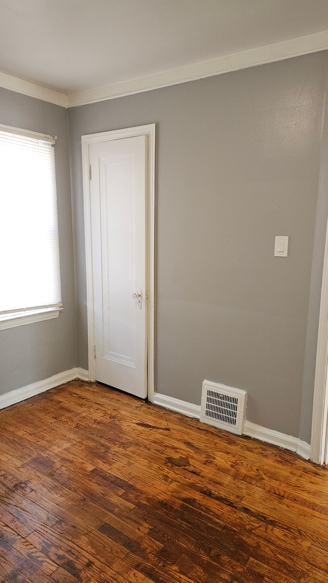 unfurnished room featuring crown molding, dark wood-type flooring, visible vents, and baseboards