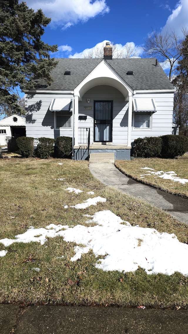 view of front facade featuring a shingled roof, a front yard, and a chimney