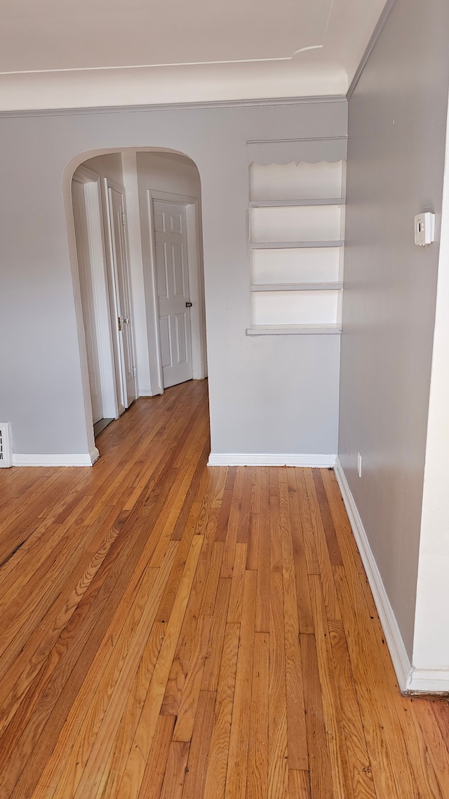 empty room featuring light wood-style floors, baseboards, visible vents, and arched walkways