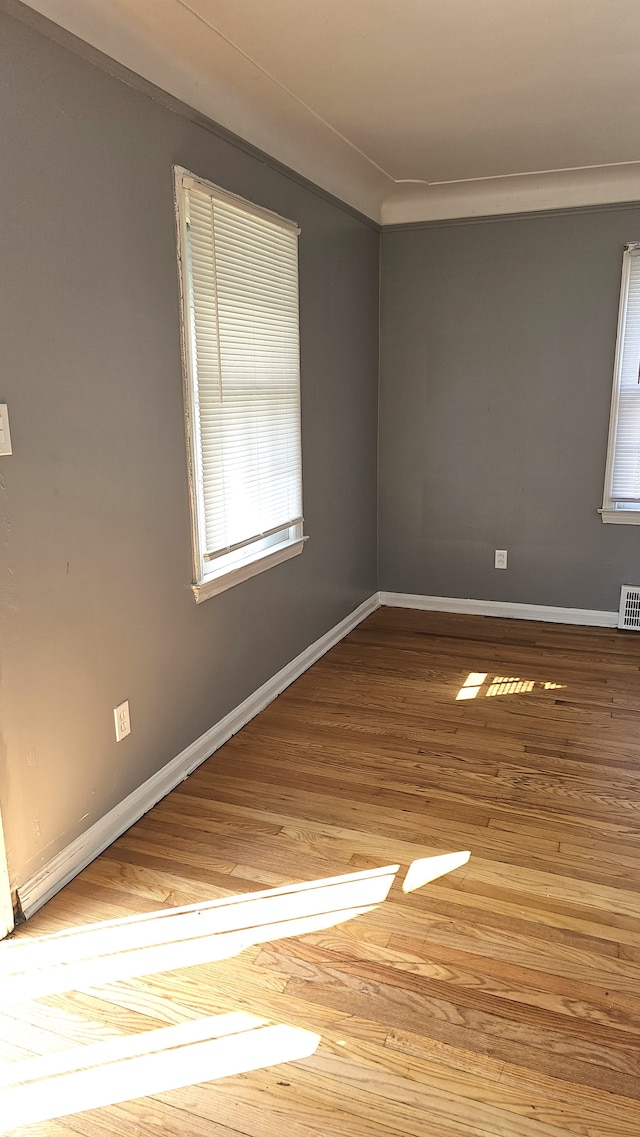 unfurnished room with ornamental molding, wood finished floors, visible vents, and baseboards