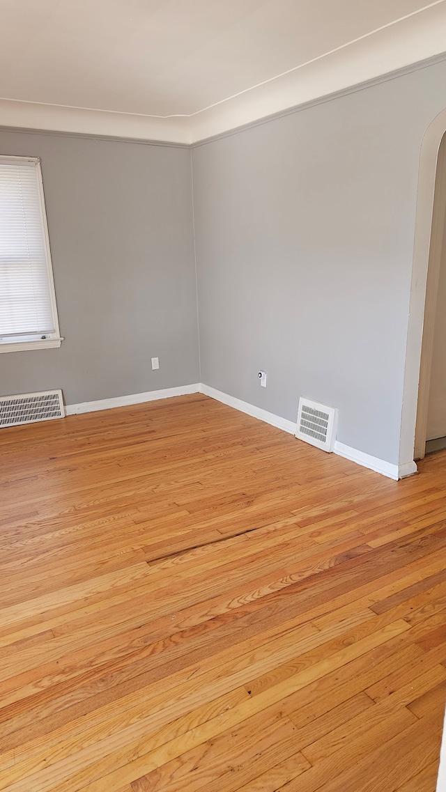 unfurnished room featuring arched walkways, light wood finished floors, visible vents, and baseboards