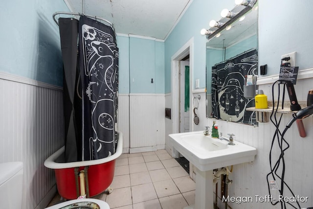 bathroom with crown molding, tile patterned floors, toilet, wainscoting, and a bath