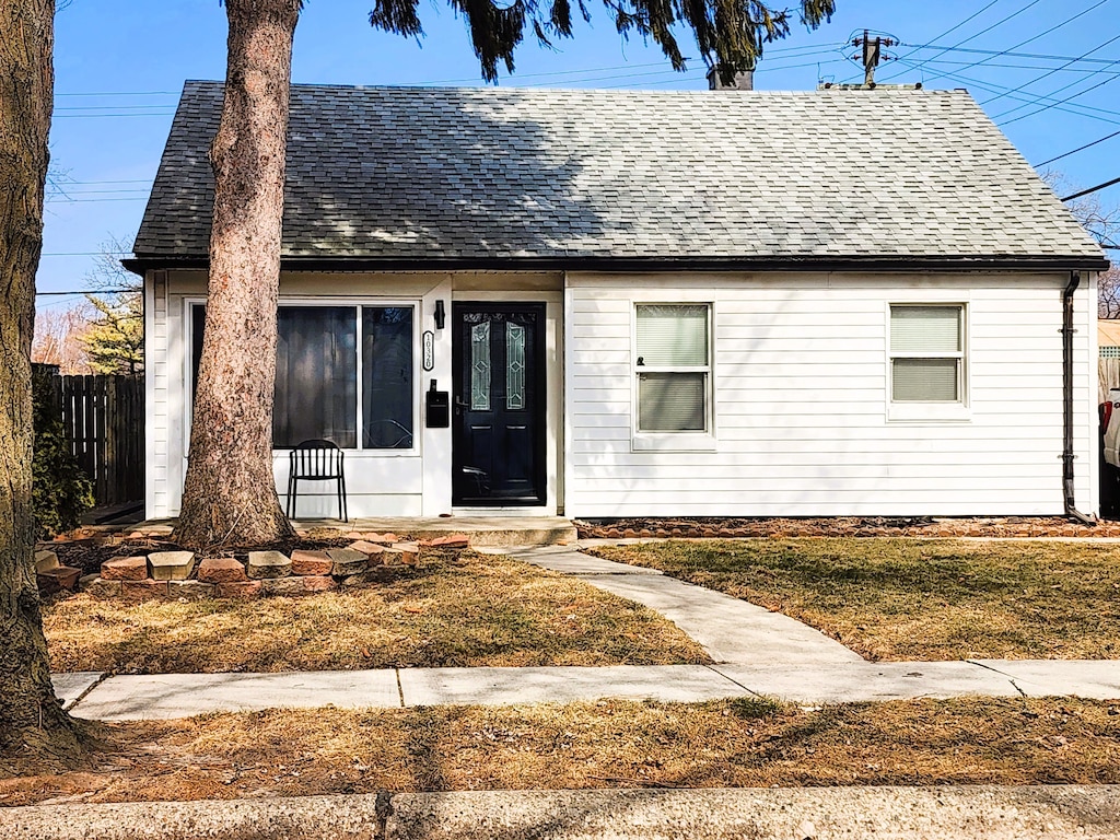 view of front facade with a shingled roof, a front yard, and fence