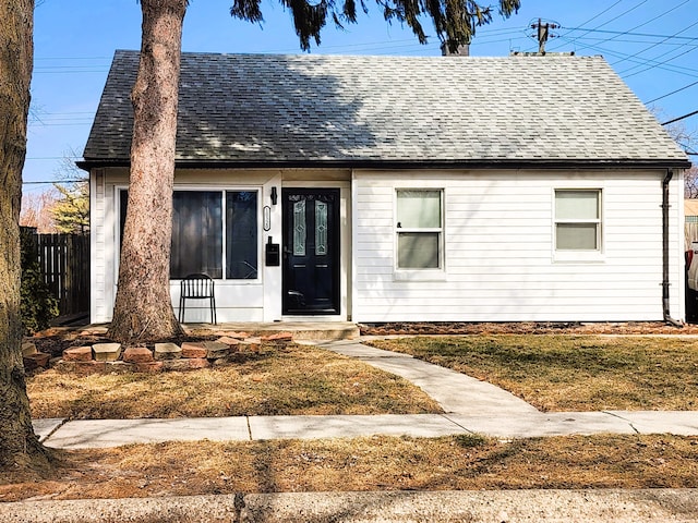 view of front facade with a shingled roof, a front yard, and fence