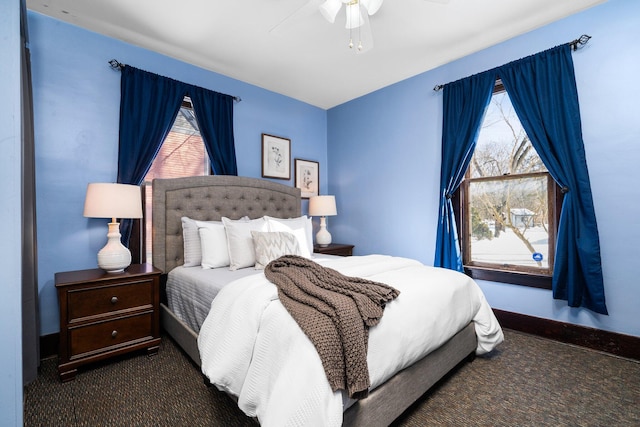 bedroom featuring multiple windows, dark carpet, a ceiling fan, and baseboards