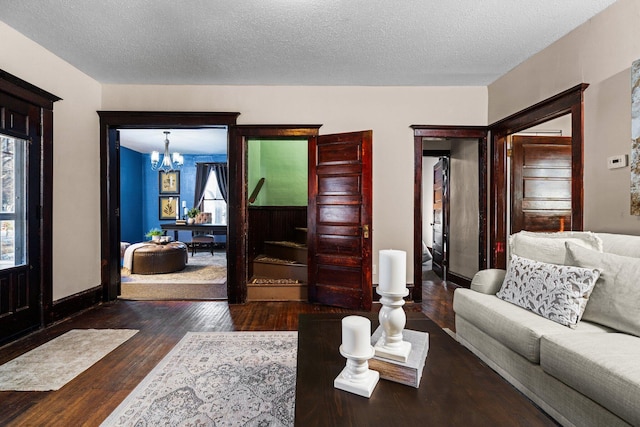 living room featuring a chandelier, dark wood-type flooring, a textured ceiling, and baseboards