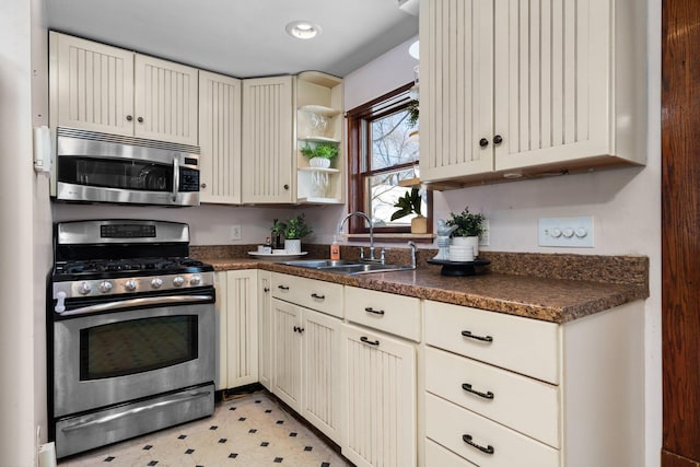 kitchen with cream cabinets, stainless steel appliances, light floors, open shelves, and a sink