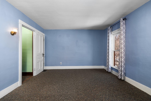 empty room featuring baseboards and dark colored carpet