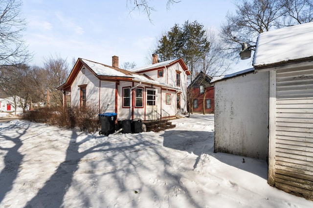 snow covered back of property with a chimney