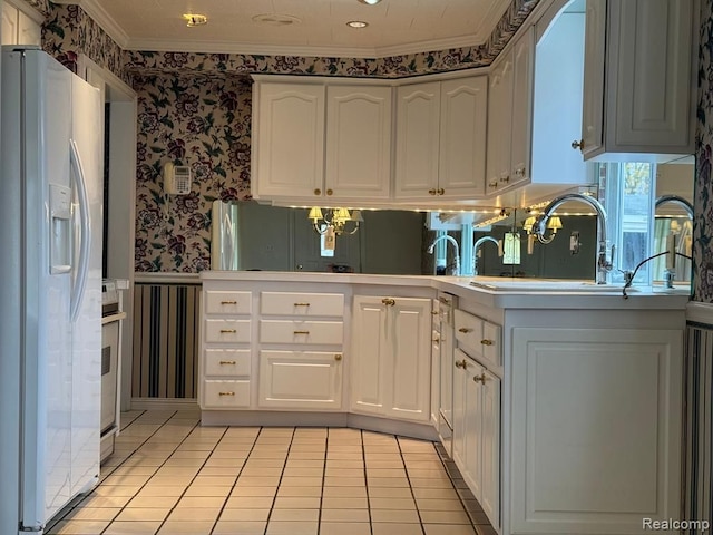 kitchen featuring a peninsula, white refrigerator with ice dispenser, white cabinetry, wainscoting, and wallpapered walls