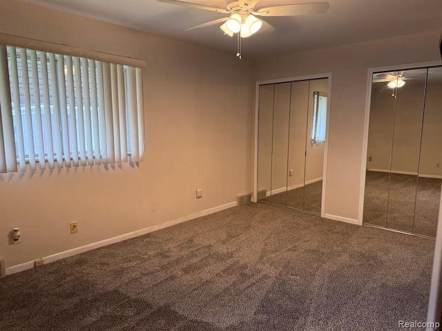 unfurnished bedroom with ceiling fan, visible vents, baseboards, multiple closets, and dark colored carpet