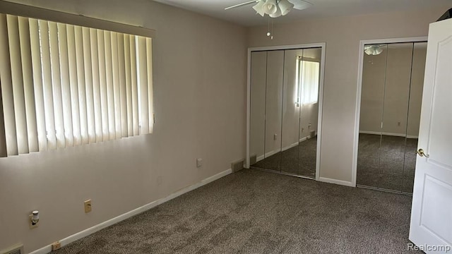 unfurnished bedroom featuring baseboards, visible vents, dark carpet, and multiple closets