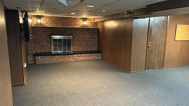 finished basement featuring carpet flooring, a fireplace, wooden walls, and a drop ceiling