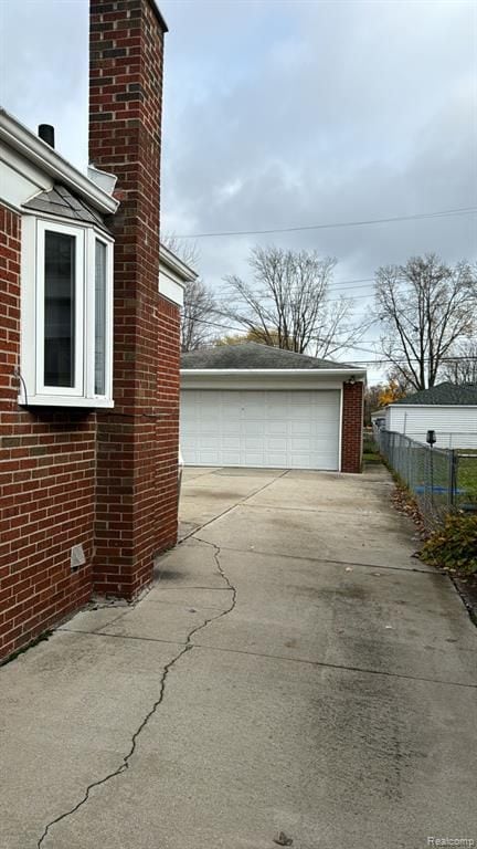 view of property exterior featuring brick siding, a chimney, a detached garage, and an outdoor structure