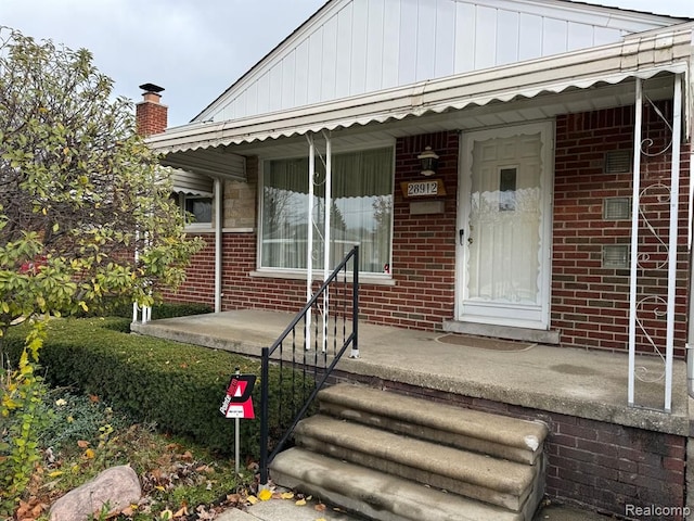 property entrance featuring covered porch, brick siding, and a chimney