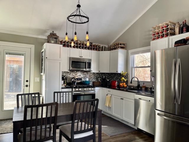 kitchen with pendant lighting, dark countertops, appliances with stainless steel finishes, a sink, and vaulted ceiling