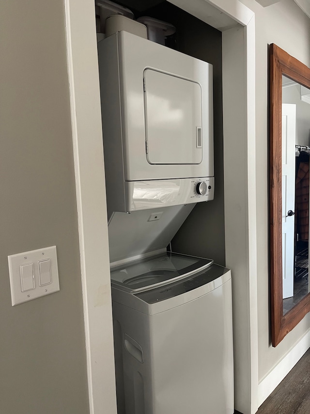 washroom with stacked washer and dryer, baseboards, laundry area, and dark wood-type flooring