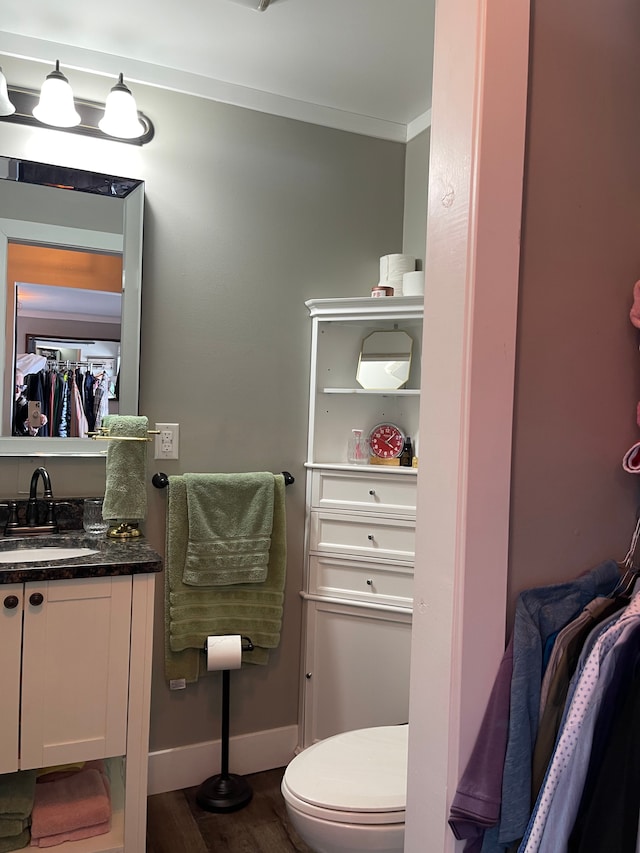 bathroom with baseboards, toilet, ornamental molding, wood finished floors, and vanity