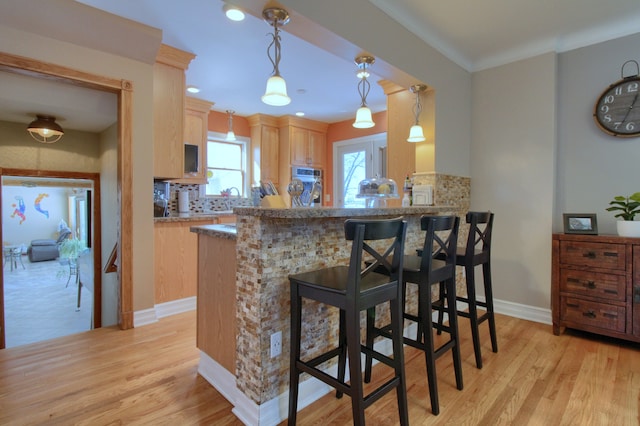 kitchen with hanging light fixtures, a peninsula, light brown cabinets, and a kitchen bar