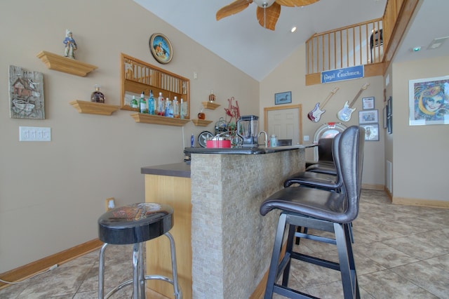 bar featuring baseboards, high vaulted ceiling, a ceiling fan, and wet bar